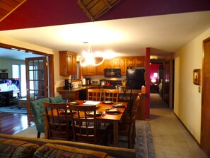 A dining area with a wooden table and chairs, a kitchen with wooden cabinets and appliances, and a living room with a sofa and a television.