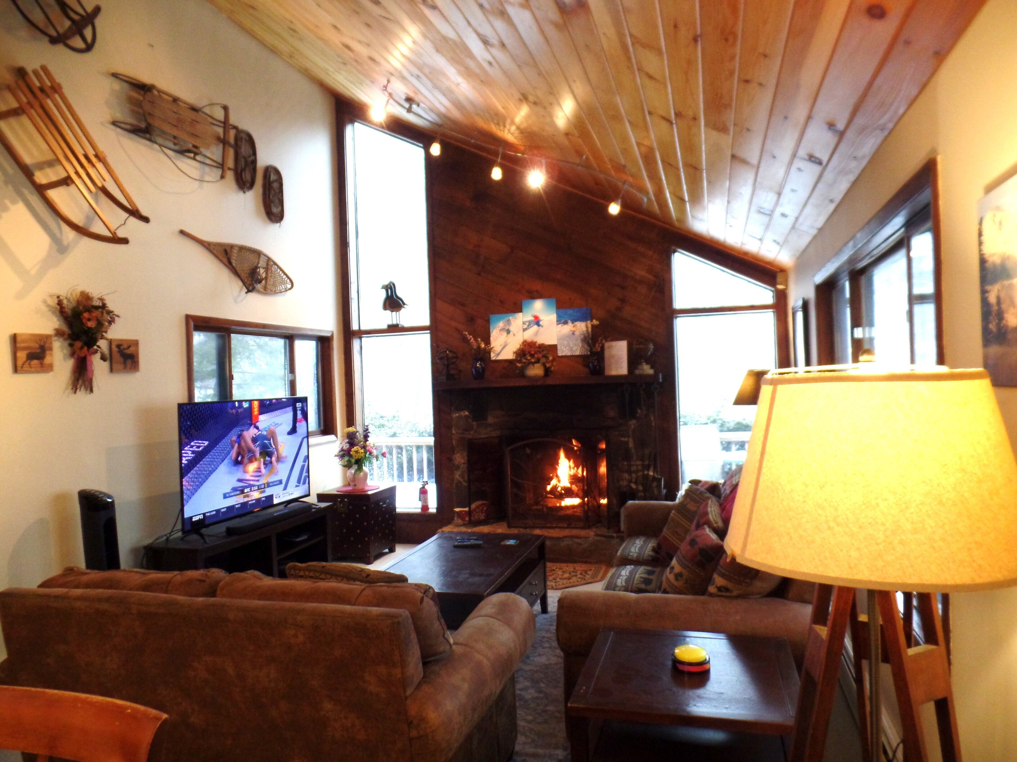 A cozy living room with a fireplace, wooden ceiling, and a television.
