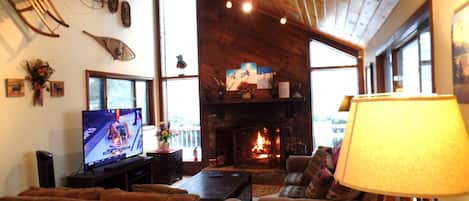 A cozy living room with a fireplace, wooden ceiling, and a television.