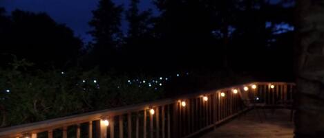 A wooden pathway with evenly spaced lights, surrounded by trees and a stone structure.