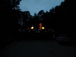 A dark outdoor area with a building in the background, surrounded by trees.
