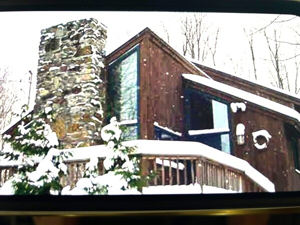 A wooden cabin with a stone chimney, large windows, and a snow-covered roof.