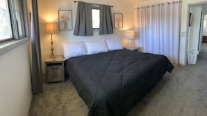 A bedroom with a large bed, two bedside tables, a window with curtains, and a wall-mounted lamp. - Garland Charmer (Spokane)