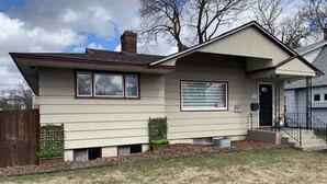 A single-story house with a front porch, a garage, and a small front yard with a wooden fence and a planter. - Garland Charmer (Spokane)