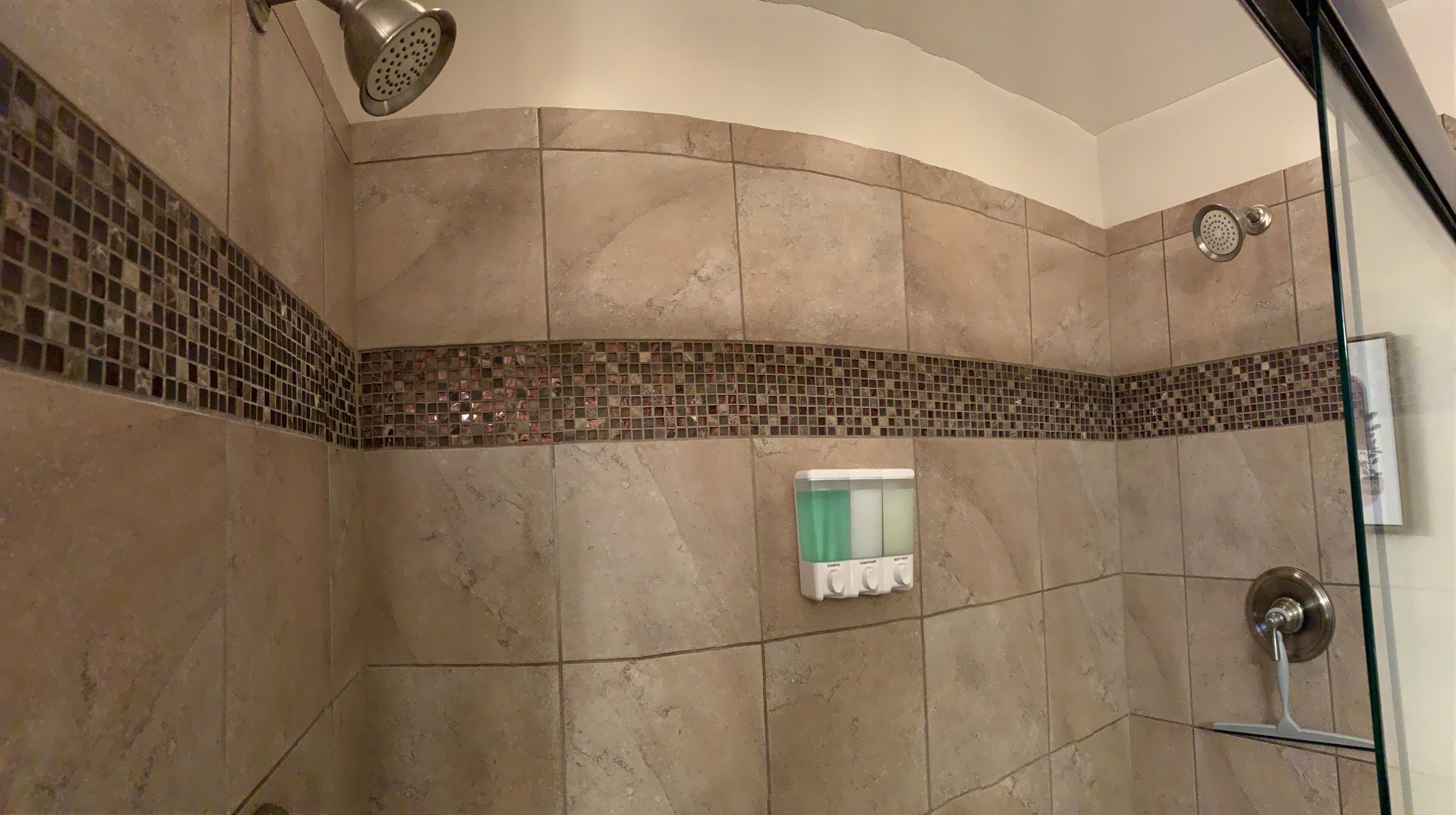 Eine Dusche mit Handbrause, Glastür und einer Fliesenwand mit Mosaikbordüre.