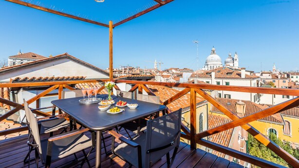 Une terrasse avec une table dressée pour le dîner, offrant une vue sur un paysage urbain avec des bâtiments historiques et un dôme.