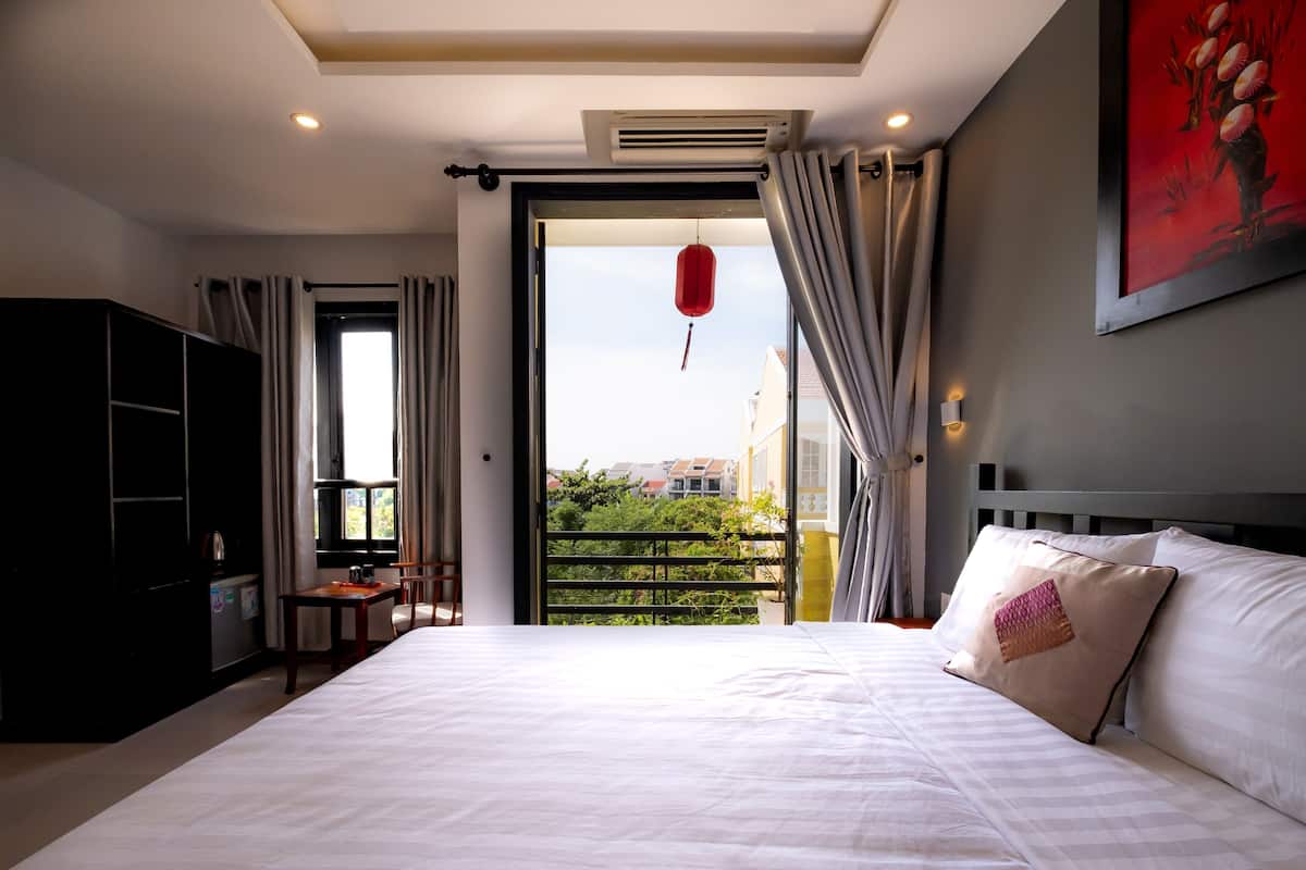 A bedroom with a bed, a desk, a wardrobe, and a view of greenery through a window.