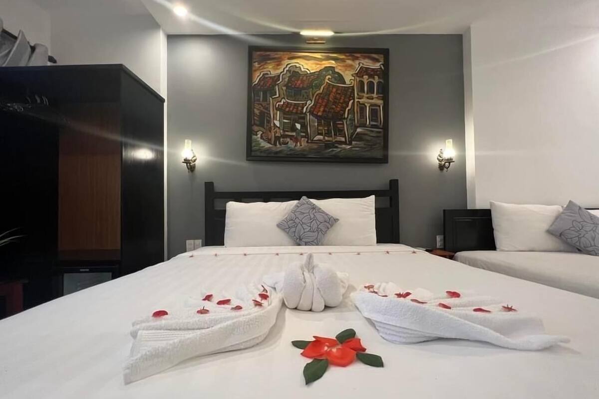 A hotel room with a large bed, two bedside tables, a headboard, a painting on the wall, and a wardrobe.