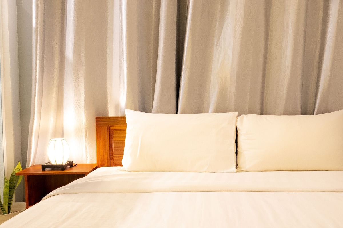 A neatly made bed with white linens, a wooden headboard, and a bedside lamp on a wooden nightstand.
