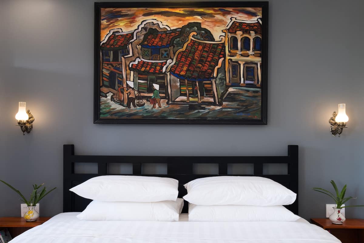 A bedroom with a bed, two wall-mounted lamps, and a painting above the bed.