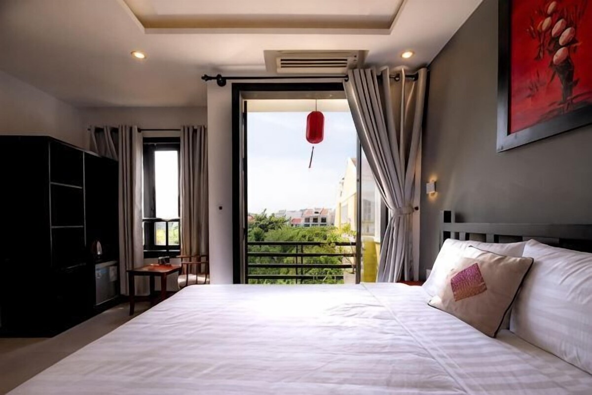 A bedroom with a bed, a wardrobe, a desk, and a view of the outdoors.