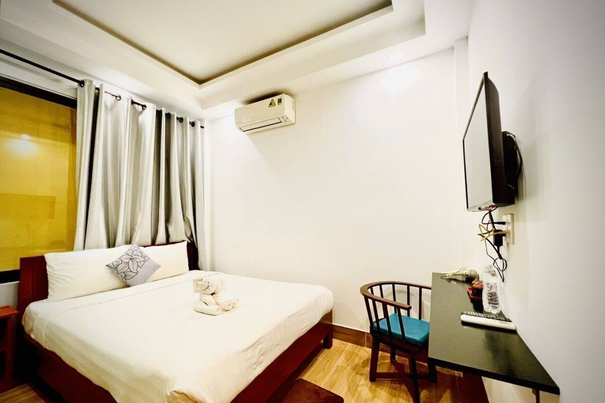 A hotel room with a bed, a desk with a computer, a chair, and a TV mounted on the wall.