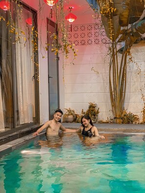 A man and a woman in a swimming pool with a decorative wall and plants in the background. - Hoi An Town Center (Da Nang)