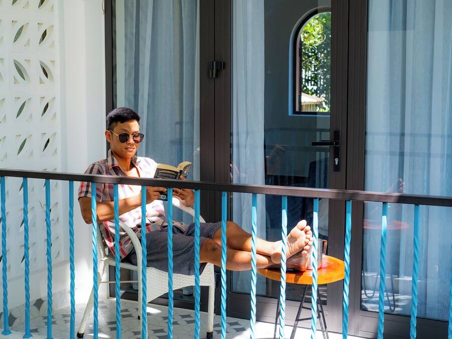 Un hombre sentado en una silla en un balcón con barandilla, leyendo un libro.