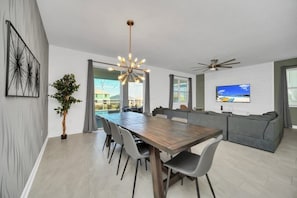 Uma sala de estar moderna com área de jantar, sofás cinza, mesa de jantar de madeira e ventilador de teto.
