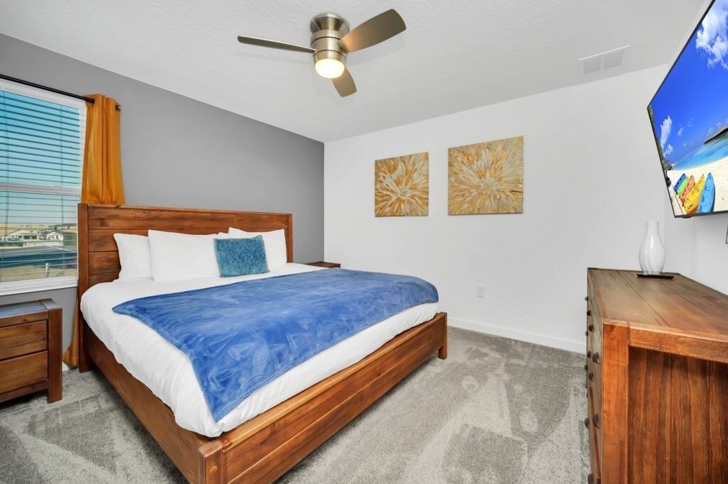 A bedroom with a wooden bed, a ceiling fan, a window with blinds, and artwork on the wall.