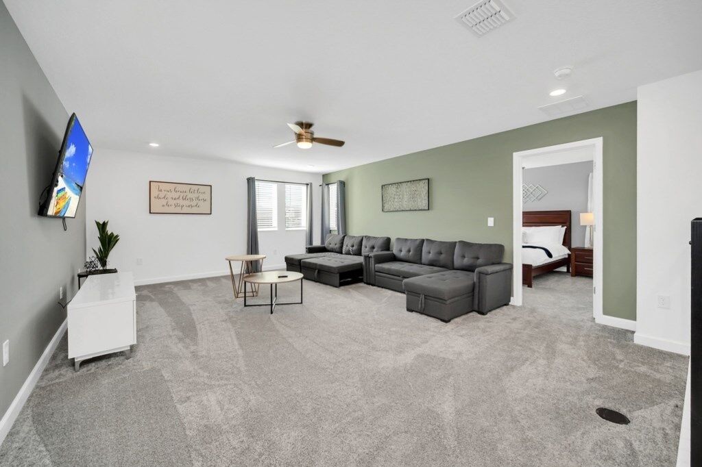 A spacious living room with a sectional sofa, a small round table, and a TV mounted on the wall.