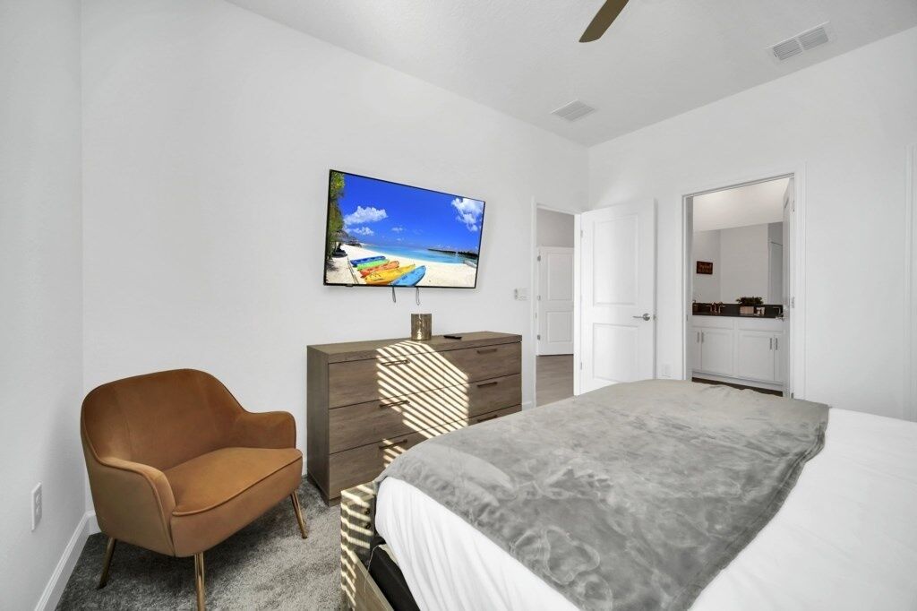 A bedroom with a bed, a TV on the wall, a dresser, and a chair.