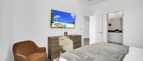 A bedroom with a bed, a TV on the wall, a dresser, and a chair.