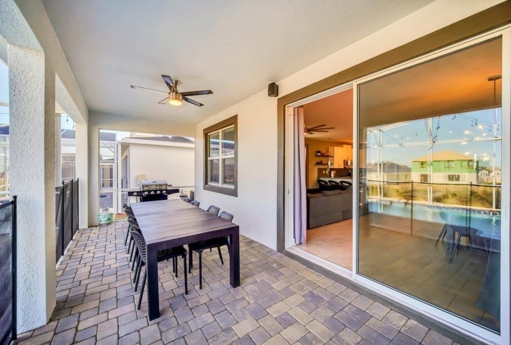 A patio area with a dining table and chairs, a ceiling fan, and a glass door leading to a pool.