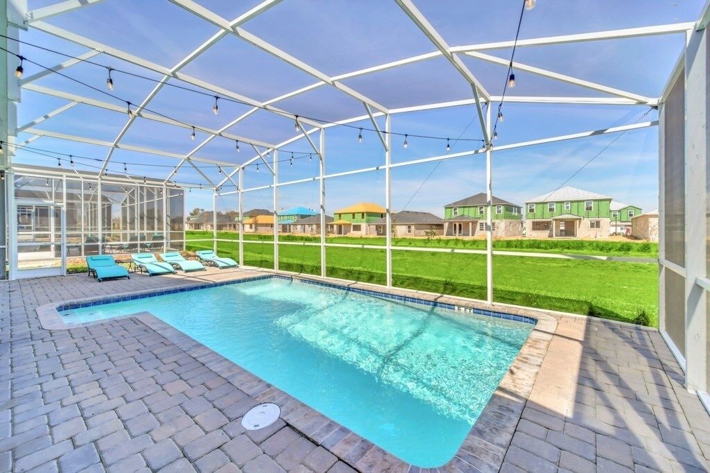 A covered swimming pool with lounge chairs and a view of houses in the background.