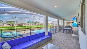 A covered outdoor area with a pool, blue seating, and a table. - 7 Bed Champions Gate 7 Bedroom Villa by RedAwning (Davenport)