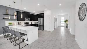A modern kitchen with a central island, black cabinets, stainless steel appliances, and a white countertop. - 7 Bed Champions Gate 7 Bedroom Villa by RedAwning (Davenport)