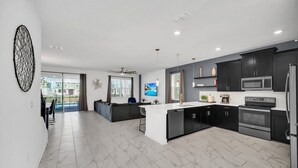 A modern kitchen with dark cabinets, a central island, and a large window. - 7 Bed Champions Gate 7 Bedroom Villa by RedAwning (Davenport)