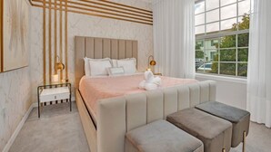 Un dormitorio moderno con una cama grande, mesitas de noche, un banco y una ventana con vistas al exterior.