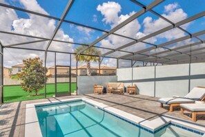En inomhuspool med väggar av genomskinligt glas, träloungestolar och utsikt över det omgivande bostadsområdet.