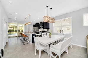 A modern kitchen with white cabinetry, a central island, and a dining area with white chairs and a table. - 5 Bedroom Resort 5 bath Pool Home With Spa! 5 Villa by RedAwning (Davenport)