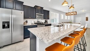 Une cuisine moderne avec des meubles de couleur sombre, des appareils en acier inoxydable, un îlot en granit et des tabourets de bar orange.