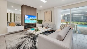 A modern living room with a flat-screen TV, a sofa, a coffee table, and a view of a swimming pool. - Many Themes For Everyone 10 Huge Bedrooms! 10 Villa by RedAwning (Kissimmee)