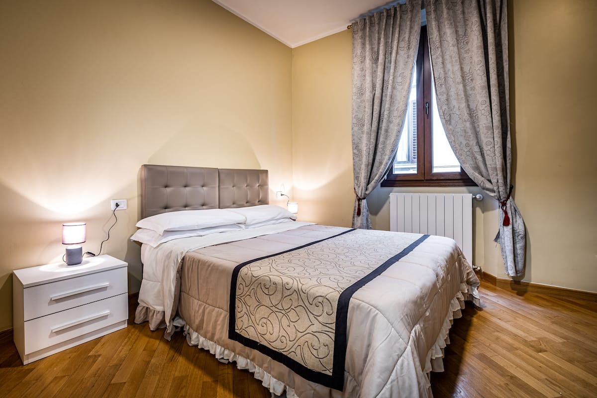 A bedroom with a bed, bedside table, lamp, and curtains.
