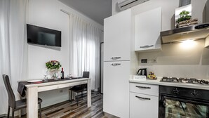A modern kitchen with a dining area, white cabinetry, a built-in oven, and a flat-screen TV mounted on the wall. - Residenza Fanti (Florence)