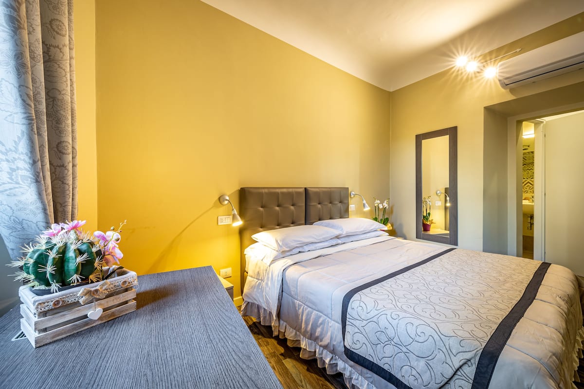 A bedroom with a bed, bedside table, lamp, and a decorative cactus arrangement.