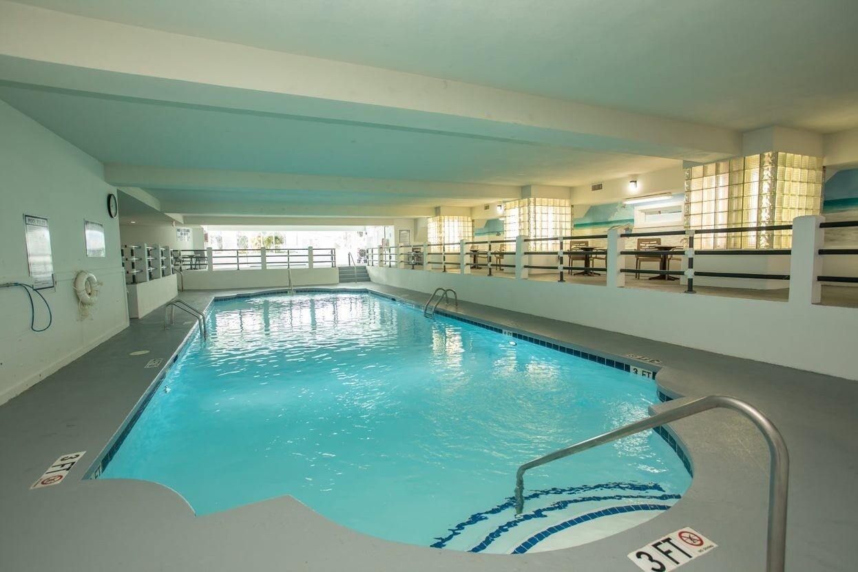 An indoor swimming pool with clear water, a 3ft depth marker, and a tiled deck area with seating.