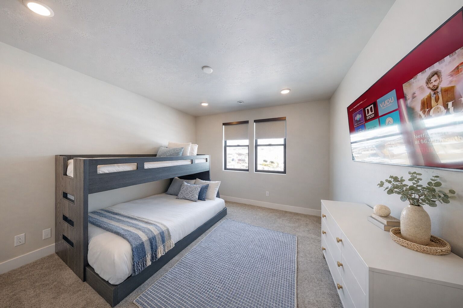 Une chambre avec un lit superposé, une commode, un tapis et un téléviseur fixé au mur.