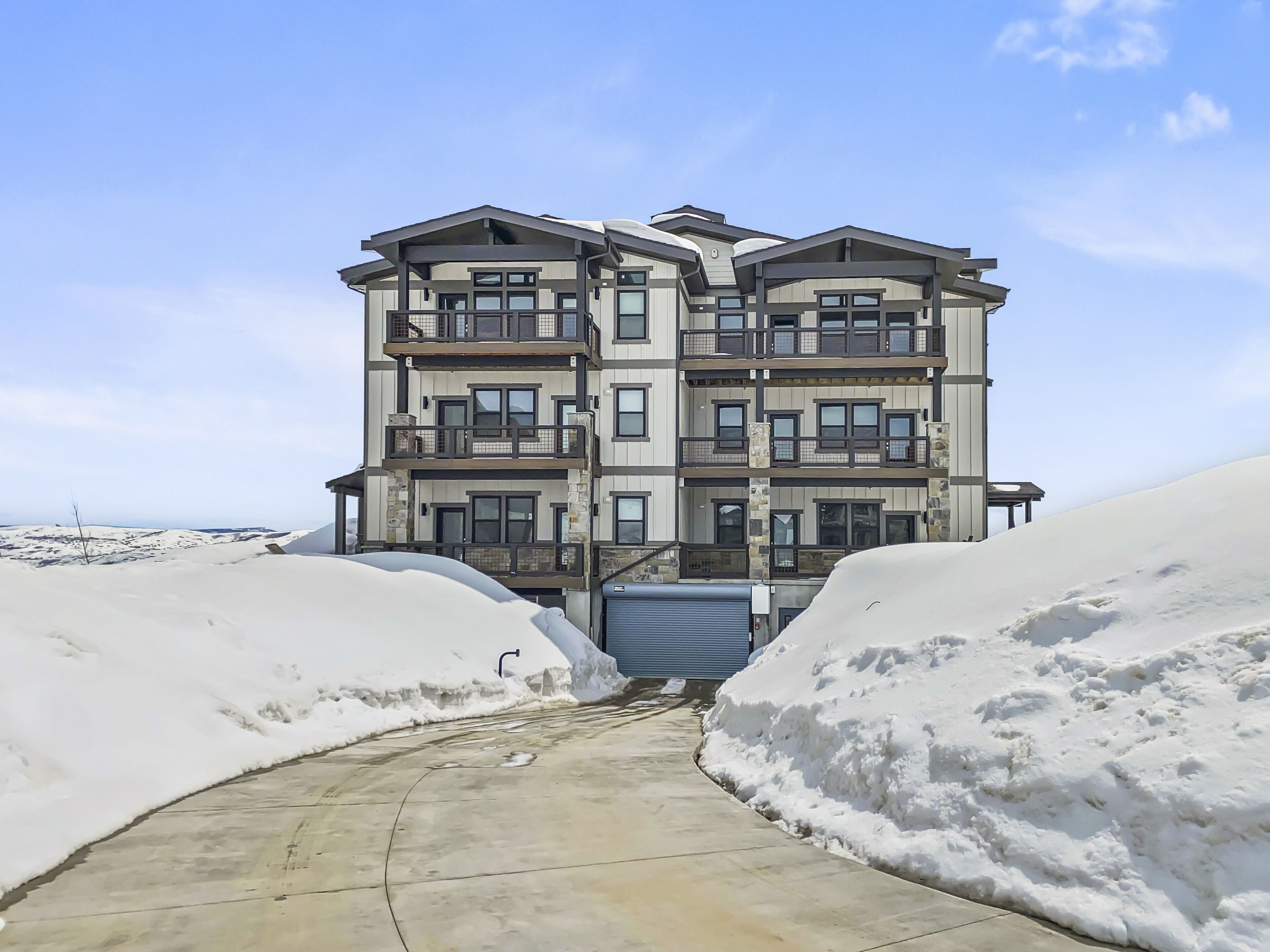 A multi-story building with balconies, a concrete pathway, and snowbanks on either side.