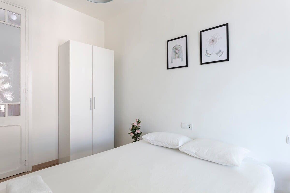 Un dormitorio con cama, armario blanco y dos cuadros en la pared.
