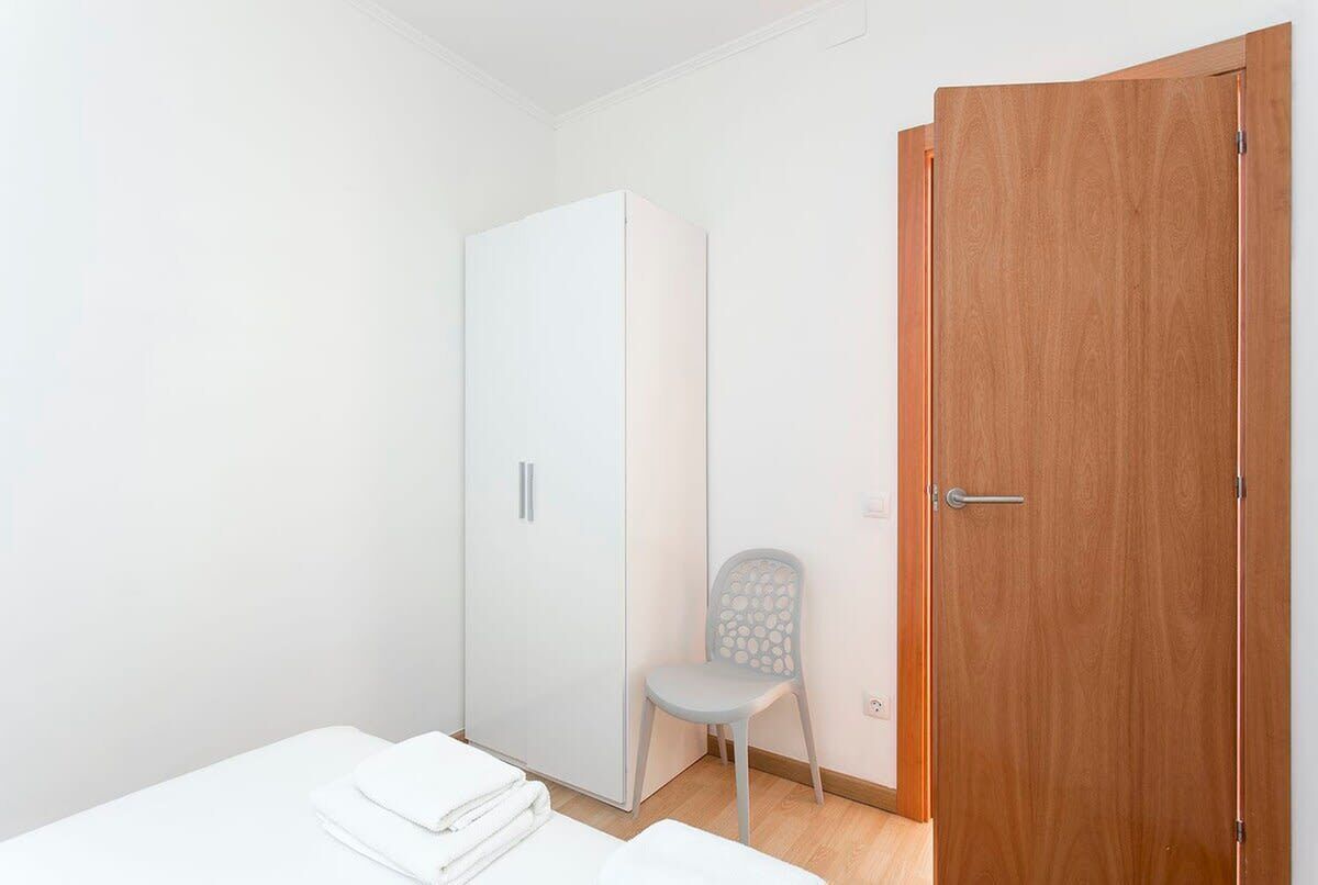 Une chambre avec une armoire blanche, une porte en bois et une chaise.