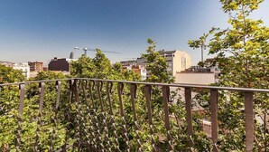 En balkon med gelænder i metal, der udover et bybillede med bygninger og en mobilkran.