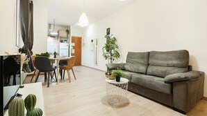 En moderne stue med en grå sofa, et spiseområde med et bord og stole, og et køkken i baggrunden.
