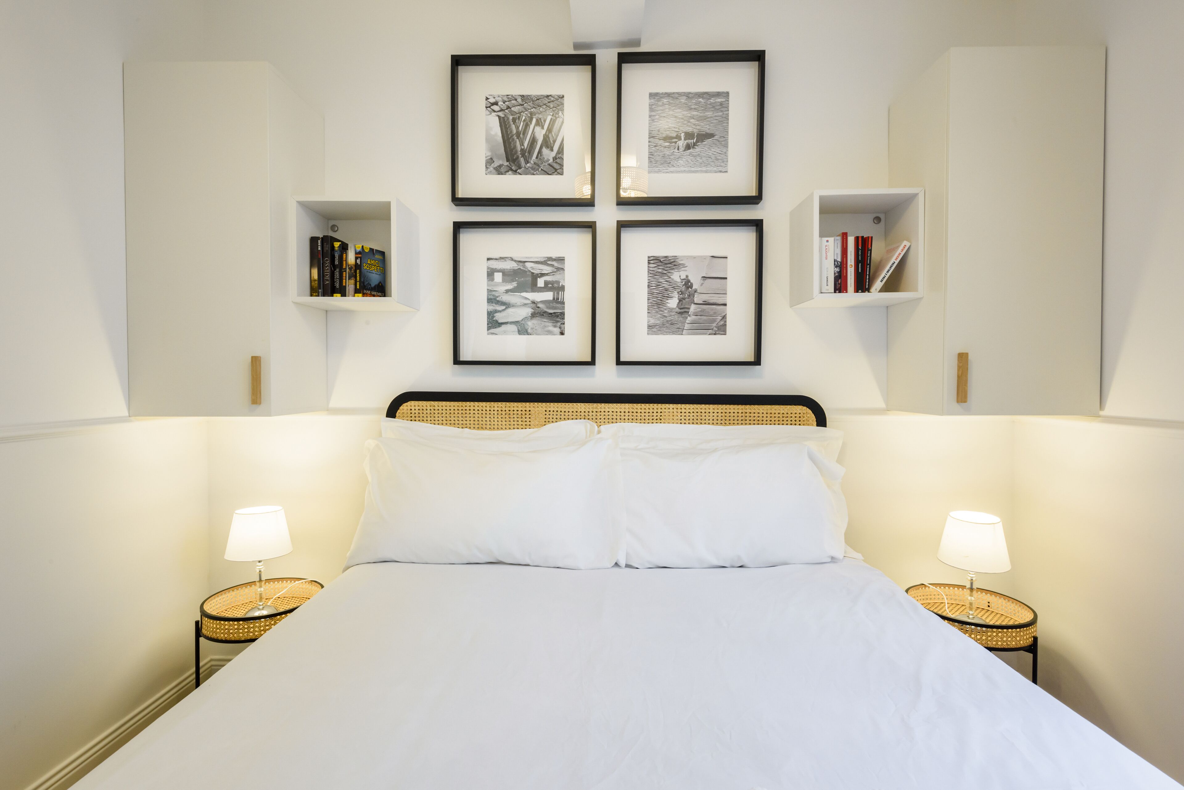 A neatly arranged hotel room with a large bed, two bedside tables with lamps, and four framed pictures on the wall.