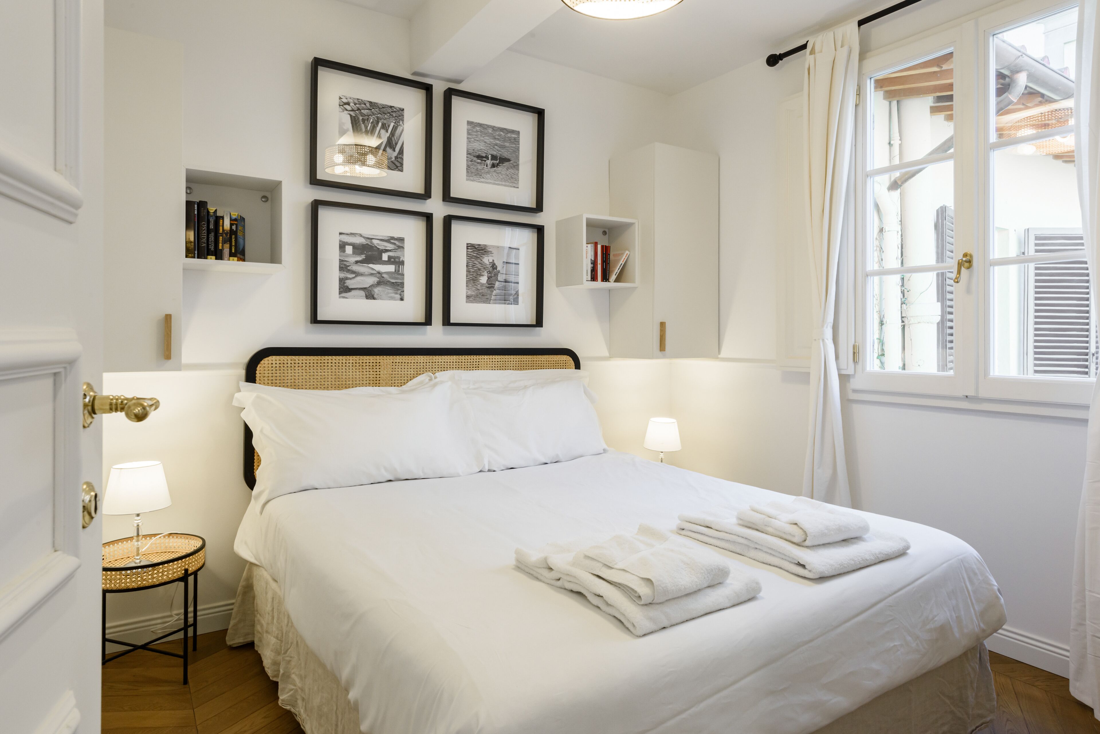 Une chambre à coucher bien rangée, avec un grand lit, des lampes de chevet, une petite table d’appoint et des tableaux encadrés accrochés au mur.