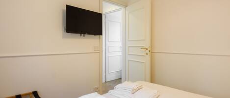 A hotel room with a bed, a TV mounted on the wall, a door leading to another room, and a towel rack.