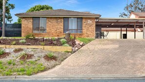 A two-story house with a brick exterior, a covered patio area, and a landscaped garden with various plants.