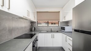 A modern kitchen with white cabinets, a stainless steel sink, a kettle, and a microwave.