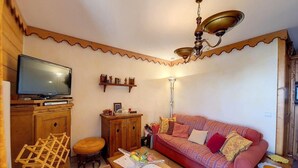 A cozy living room with a television, wooden furniture, a patterned sofa, and a ceiling light fixture. - Ski-in/ski-out & foot of the slopes, 2nd floor, balcony, 45m², Les Menuires (Les Menuires)
