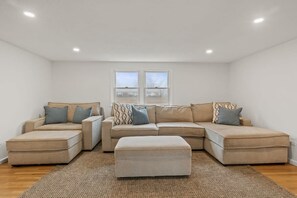 A living room with a sectional sofa, ottoman, and a large window.